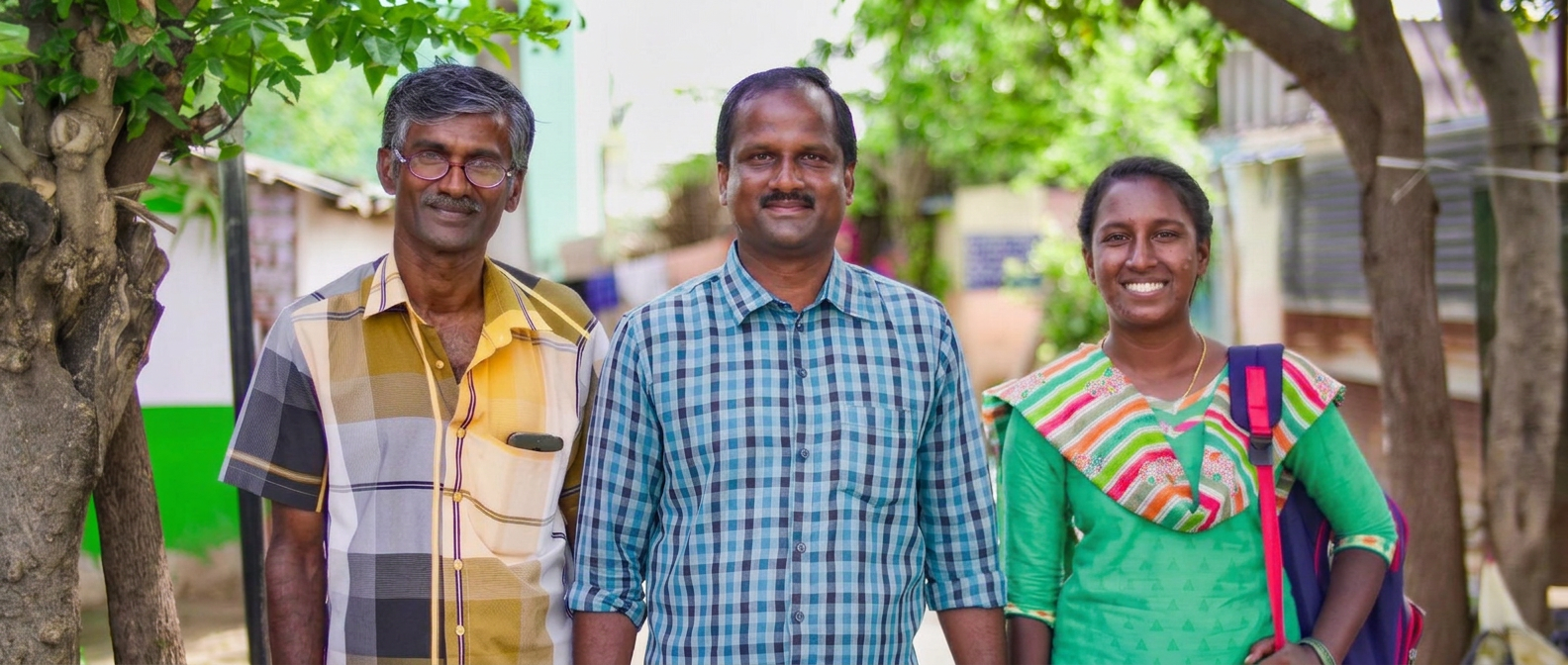Three smiling JFA Bible workers standing together in a village street